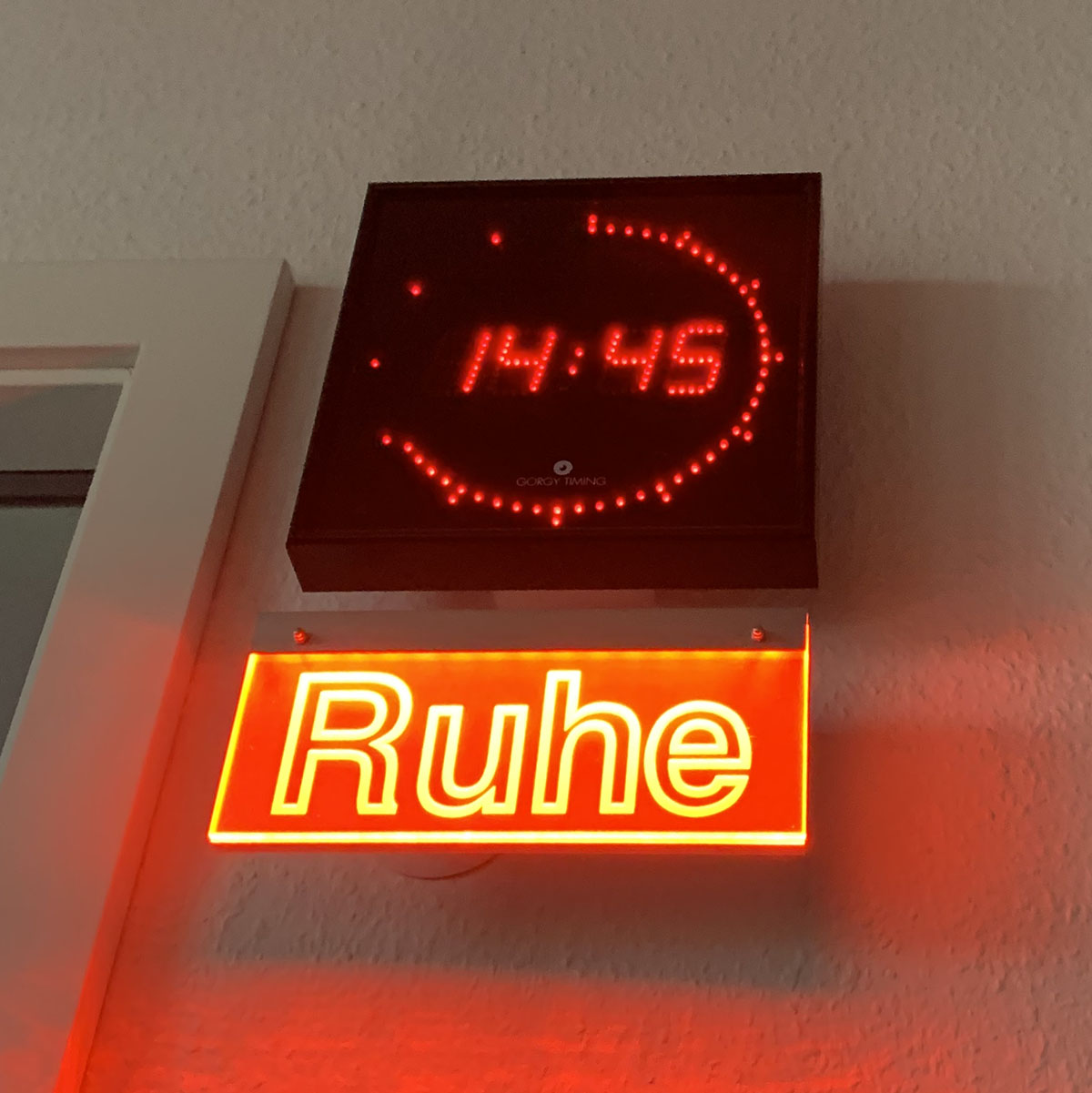 Rot leuchtendes Schild "Ruhe", mit einer Digitalen Wanduhr darüber.