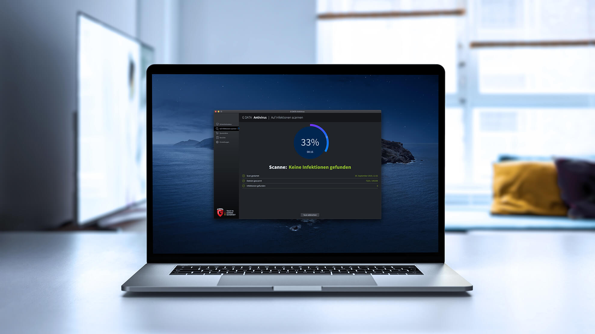 Auf dem Foto kann man im Hintergrund unscharf ein Sofa und einen Fernseher erkennen. Im Vordergrund ist ein Schreibtisch abgebildet auf dem ein Macbook steht. Auf dem Display ist die Softwareoberfläche der G DATA Antivirus für Mac abgebildet. Dort steht, dass keine Infektionen gefunden wurden.