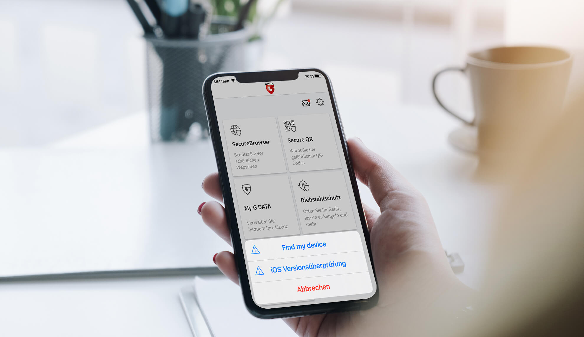 Auf dem Foto kann man im Hintergrund unscharf einen Schreibtisch mit Stiften erkennen. Im Vordergrund ist eine Hand zu sehen, die ein Iphone hält. Auf dem Display ist die Softwareoberfläche der G DATA Mobile Security abgebildet.