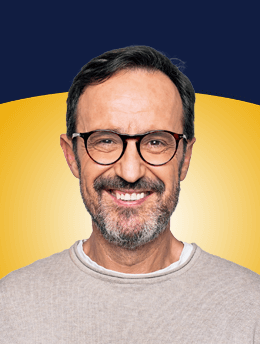 Porträt eines lächelnden Mannes mit Brille vor gelb-blauem Hintergrund